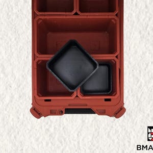 Puede incluir: Un organizador de almacenamiento rojo con múltiples compartimentos, incluyendo dos bandejas cuadradas negras. El organizador tiene una superficie texturizada y está diseñado para un almacenamiento eficiente. El logo "BMAX3D" es visible en la esquina inferior derecha.