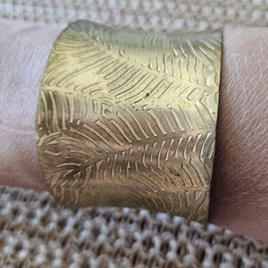 May include: A gold-toned metal cuff bracelet with a textured leaf pattern.