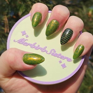 May include: Green and gold nail art with a circuit board design. One nail features a binary code pattern. The nails are on a light green circle with the text "Merbirb Sisters" in purple.