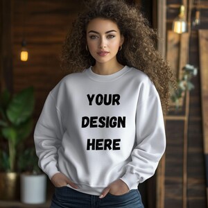 Può includere: Una felpa bianca con la scritta "YOUR DESIGN HERE" in nero. La felpa è a girocollo. La persona nell'immagine indossa la felpa e ha le mani in tasca.