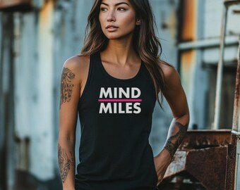 May include: Black tank top with the words "MIND MILES" in white, with a pink line underneath. The tank top is sleeveless and has a scoop neck. The background is a weathered metal structure.