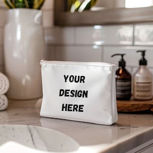 May include: White zippered makeup bag with the text "YOUR DESIGN HERE" printed in black.