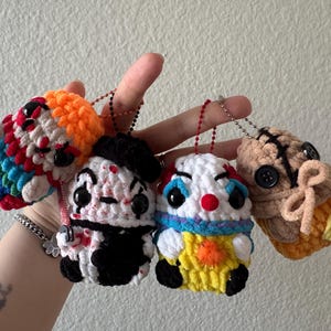 May include: Four handmade crochet doll ornaments. The dolls are designed to resemble horror movie characters, with colourful yarn and button eyes. Each doll has a keychain attached.