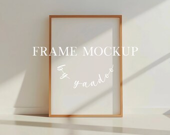 May include: A light wood frame mockup with a white background. The frame is standing on a white surface. The text "FRAME MOCKUP by y-andoo" is written in white on the frame.