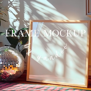 Op de afbeelding: Een mockup van een licht houten frame met een witte achtergrond. Het frame staat op een gestreept tapijt met een discobal op de voorgrond. De tekst "FRAME MOCKUP" is in wit op het frame geschreven.