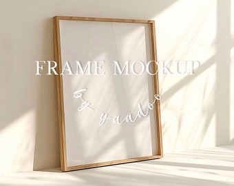 May include: A wooden frame mockup with a white background. The frame is sitting on a white surface with a shadow cast from the frame. The text "FRAME MOCKUP" is written in white on the frame.