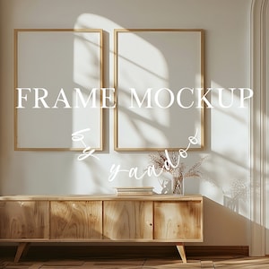 Può includere: Due cornici vuote con cornice in legno chiaro, appese a una parete bianca sopra un mobile in legno chiaro. Il mobile ha quattro ante e poggia su quattro gambe. Il mobile è davanti a una porta bianca con una modanatura decorativa. Il testo "FRAME MOCKUP by yaado" è scritto in bianco sul muro.