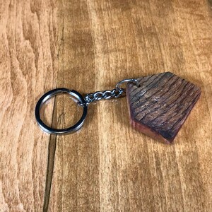 May include: A wooden keychain with a natural wood grain pattern and a silver metal key ring. The keychain is shaped like a pentagon.