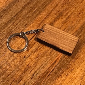 May include: A wooden keychain with a silver key ring. The keychain is rectangular and has a natural wood grain finish.
