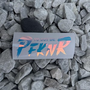 May include: A gray sticker with a sunset reflected in the letters "PEKNR" and the text "YO SOY DE" above the letters.