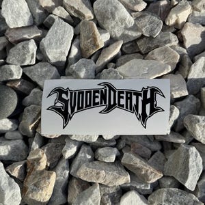 May include: A white sticker with the black text "SUICIDAL DEATH" in a stylized font. The sticker is on a background of gray rocks.