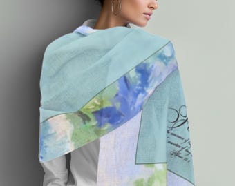 May include: A light blue scarf with a watercolor floral design in shades of blue, green, and white. The scarf has a fringed edge and a printed script with the words "...in the assurance of..." and "...Hebrews 11:1".