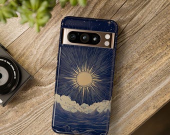 May include: A navy blue phone case featuring a gold sunburst design over a landscape of clouds and mountains. The case has a gold camera bar and is on a wooden surface. A camera and plant are in the background.