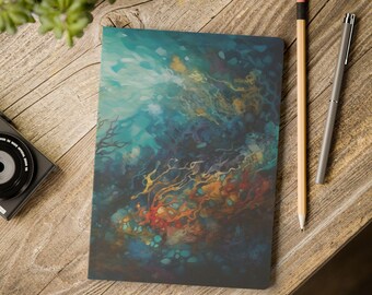 May include: A closed notebook with an abstract design in shades of blue, teal, orange, and red. A pencil and a pen are next to the notebook on a wooden surface. A small plant and a camera are also visible.