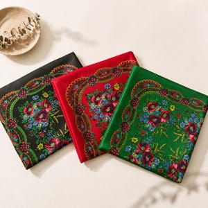 May include: Three colorful square scarves with floral patterns. One is black, one is red, and one is green. Each scarf features a detailed border and a central design of red, blue, and yellow flowers.