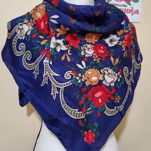 May include: A square, navy blue scarf with a floral pattern. The scarf features red, white, and orange roses and other flowers. The edges have a decorative scroll design. The scarf is made of a silky material.