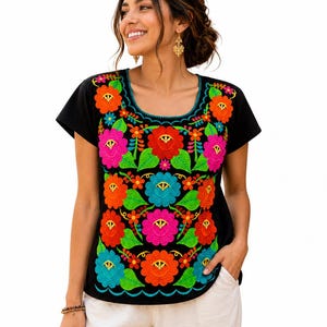 May include: Black embroidered top with a vibrant floral design in shades of orange, pink, blue, and green. The short-sleeved shirt features a scoop neckline and a scalloped hemline. The colorful embroidery creates a striking contrast against the black fabric.