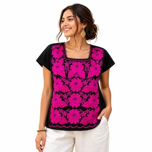 Puede incluir: Top negro de manga corta con cuello cuadrado y bordado floral rosa vibrante. El bordado cubre la parte delantera y el escote de la blusa. La blusa se combina con pantalones blancos.
