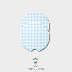 May include: Two round car coasters with a light blue and white gingham pattern. One coaster has a small notch. The coasters are from Salty Haven, as indicated by the logo at the bottom.