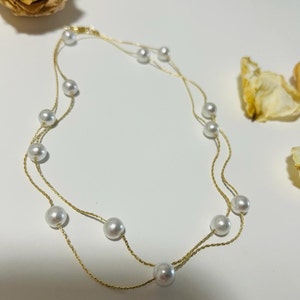 Peut inclure: Un collier délicat en chaîne dorée avec des perles blanches. Le collier est composé de deux rangs de chaîne et comporte neuf perles au total.