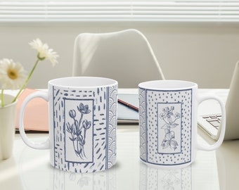 May include: Two white ceramic mugs with blue floral designs. The mug on the left has a blue floral design with a white border. The mug on the right has a blue floral design with a white border and a blue polka dot background.