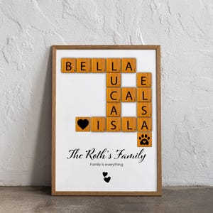 May include: A framed family name art print. The names Bella, Lucas, and Isla are spelled out with wooden letter tiles. The print includes a black heart, paw print, and the text "The Roth's Family" and "Family is everything".