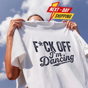 Könnte beinhalten: Ein weißes kurzärmeliges T-Shirt mit dem dunkelblauen Text F*CK OFF I'm Dancing auf der Vorderseite. Die Schrift verwendet eine Kombination aus einer fetten serifenlosen Schriftart für die erste Zeile und einer Schreibschrift für die zweite.