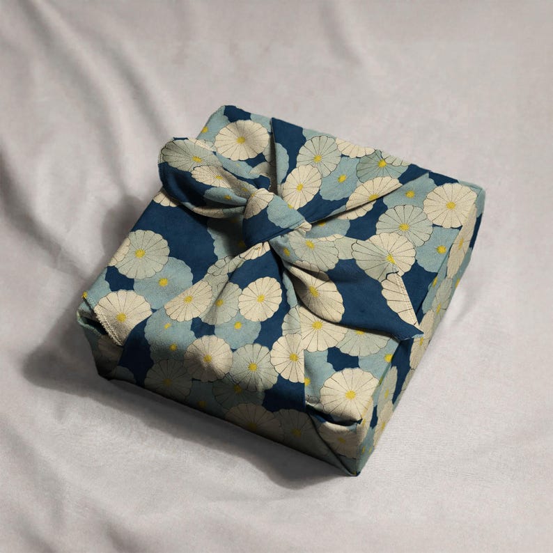 Beautifully wrapped gift showcasing a unique and sustainable Japanese Furoshiki technique, using floral fabric adorned with ivory and light blue chrysanthemums on a rich navy background. Tied with an elegant knot for a thoughtful, one-of-a-kind presentation.