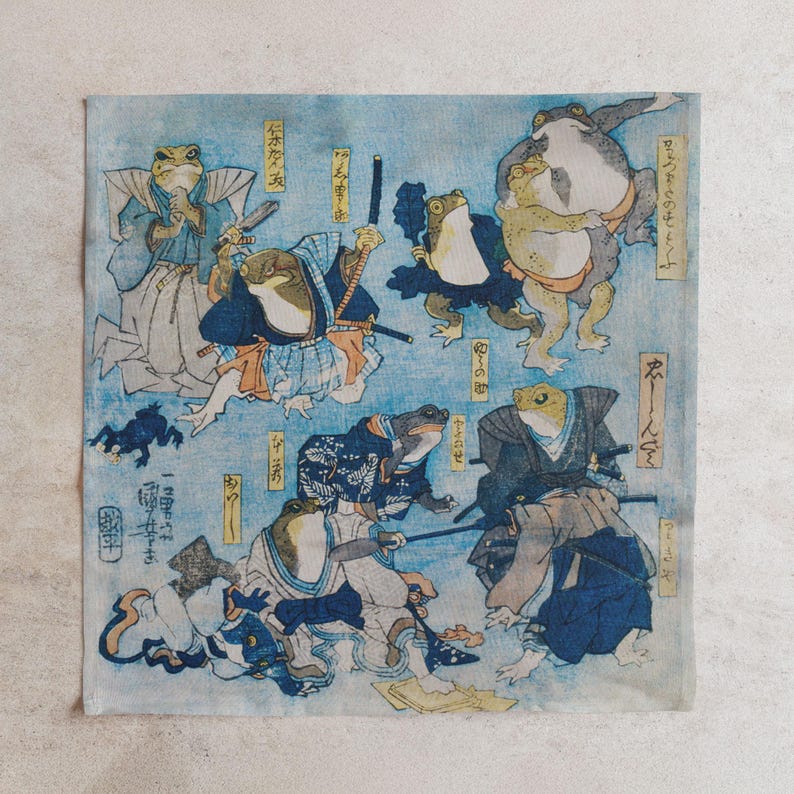 May include: A light blue square cloth with a Japanese woodblock print of samurai frogs. The print shows frogs in traditional clothing, wielding swords and in action poses. The background is a light blue wash, with Japanese text.
