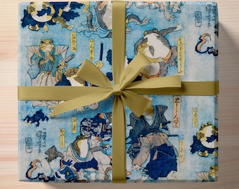 May include: A blue and white wrapping paper with a Japanese design featuring frogs in various poses. The paper is tied with a gold ribbon.