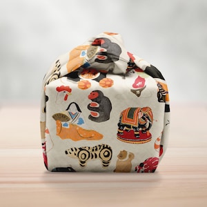 May include: A beige fabric bag with a repeating pattern of colorful illustrations of animals and figures. The bag features a monkey, elephant, bear, and other designs. The bag is sitting on a wooden surface.