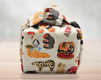 May include: A beige fabric bag with a repeating pattern of colorful illustrations of animals and figures. The bag features a monkey, elephant, bear, and other designs. The bag is sitting on a wooden surface.