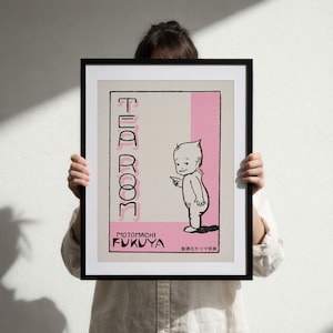 May include: A framed print featuring a beige background with a pink vertical stripe. The text reads TEA ROOM, MOTOMACHI FUKUYA, and Japanese characters. A black and white illustration of a small, bald, standing figure points to the left.