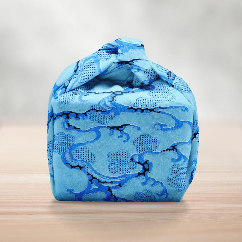 Pu&ograve; includere: Una borsa di stoffa blu con un motivo a nuvole e onde. La borsa &egrave; annodata in alto, creando una forma unica. Il design presenta uno sfondo azzurro con accenti blu scuro e neri.