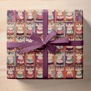 Puede incluir: Cinta morada atada alrededor de una caja de regalo con un dise&ntilde;o de papel de regalo de im&aacute;genes repetidas de luchadores de sumo en varias poses. Los luchadores llevan ropa tradicional de colores.