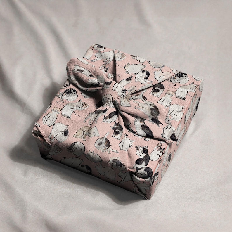 Pu&ograve; includere: Un regalo quadrato avvolto in tessuto rosa con un motivo ripetuto di illustrazioni di gatti in bianco e nero. Il tessuto &egrave; legato con un fiocco abbinato, creando una presentazione decorativa e unica.