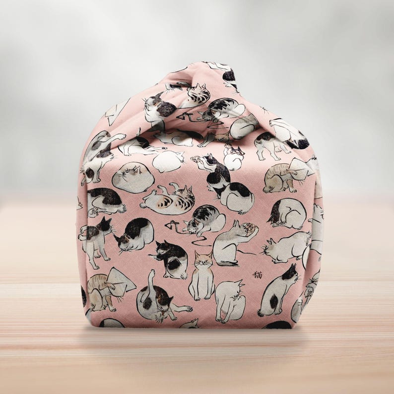 Pu&ograve; includere: Una borsa di stoffa rosa con un motivo ripetuto di illustrazioni di gatti in bianco e nero in varie pose. La borsa &egrave; annodata in alto, creando una forma unica. I gatti sono raffigurati in varie posizioni, come seduti, che si allungano e giocano.