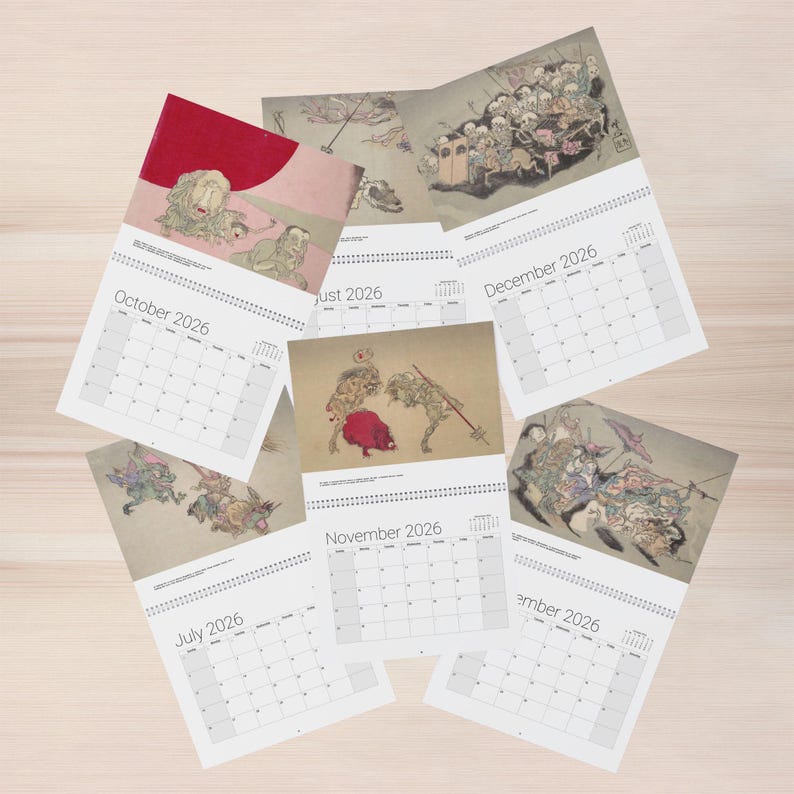 May include: A collection of 2026 calendars featuring traditional Japanese art. Each calendar displays a different month, with illustrations of mythical creatures and historical scenes. The calendars are arranged on a light wood surface.