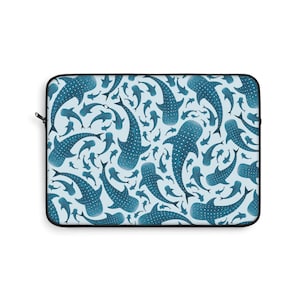 May include: A rectangular laptop sleeve featuring a repeating pattern of blue whale sharks on a light blue background. The whale sharks are detailed with white spots and varying sizes. The sleeve has a black zipper and trim.