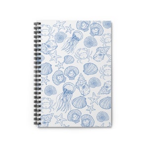 Pode incluir: Um caderno espiral branco com um padrão de conchas marinhas azul e branco. O padrão inclui estrelas do mar, conchas, medusas e caranguejos.