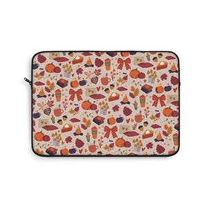 May include: A laptop sleeve with a repeating pattern of autumn-themed illustrations. The design includes pumpkins, fall leaves, coffee cups, pie slices, bows, and mushrooms in shades of orange, brown, and beige.