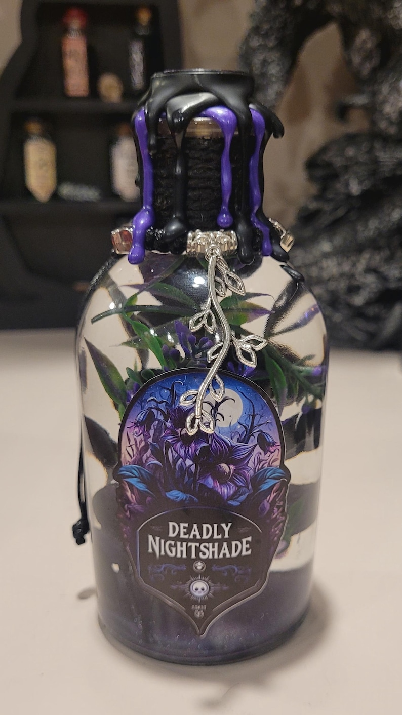 May include: A glass bottle with a black and purple wax seal, a silver charm, and a sticker that says "Deadly Nightshade". The bottle is filled with a clear liquid and green foliage.