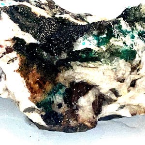 May include: A close-up of a rough, white rock with green, black, and brown mineral deposits. The rock has a natural, organic texture.