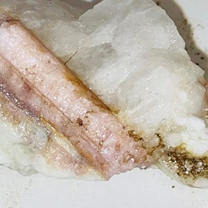 Peut inclure: Un spécimen minéral rose et blanc avec une surface rugueuse et texturée. Le minéral est incrusté dans une matrice blanche.