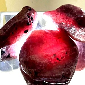 May include: Three large, irregularly shaped, pink and purple gemstones. The gemstones are smooth and polished, with a translucent appearance.