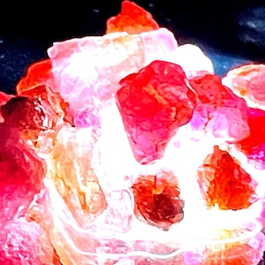 May include: A cluster of pink and red crystals with a white, glowing centre. The crystals are arranged in a random, organic pattern, creating a visually appealing and unique display.