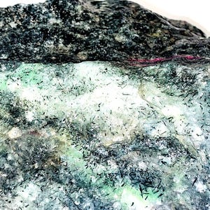 May include: A close-up of a rough, gray, green, and pink rock with black streaks. The rock has a variety of textures and colors.