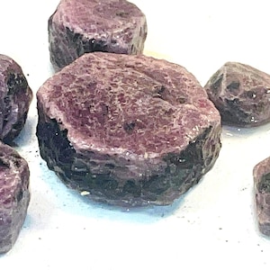 Puede incluir: Seis piedras preciosas de rubí rosa en bruto con un interior oscuro, casi negro. Las piedras preciosas son de varios tamaños y formas.