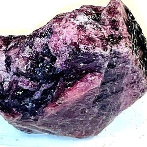 May include: A large, rough, purple and black gemstone with a crystalline structure. The gemstone is approximately 5 cm in size.