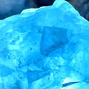 May include: A large, blue, crystalline rock with a rough, textured surface. The rock is illuminated from below, highlighting its intricate details.